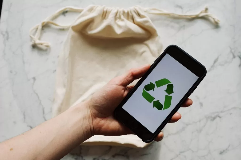 A hand holding a phone with the recycling icon showing on the screen