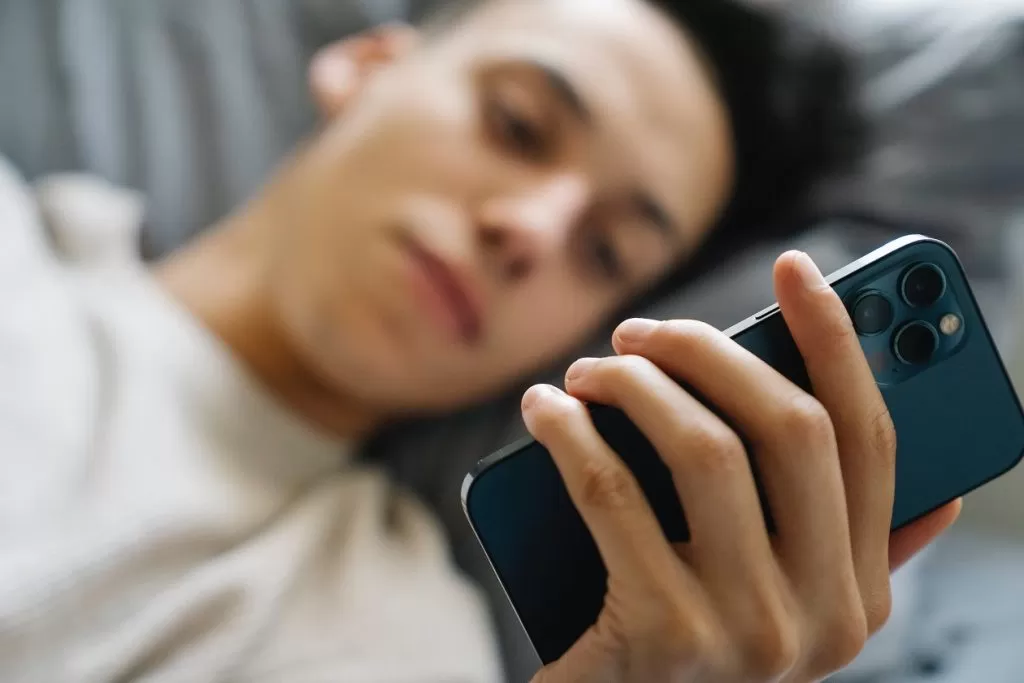 A young man looking at his phone while laying down, with a serious facial expression